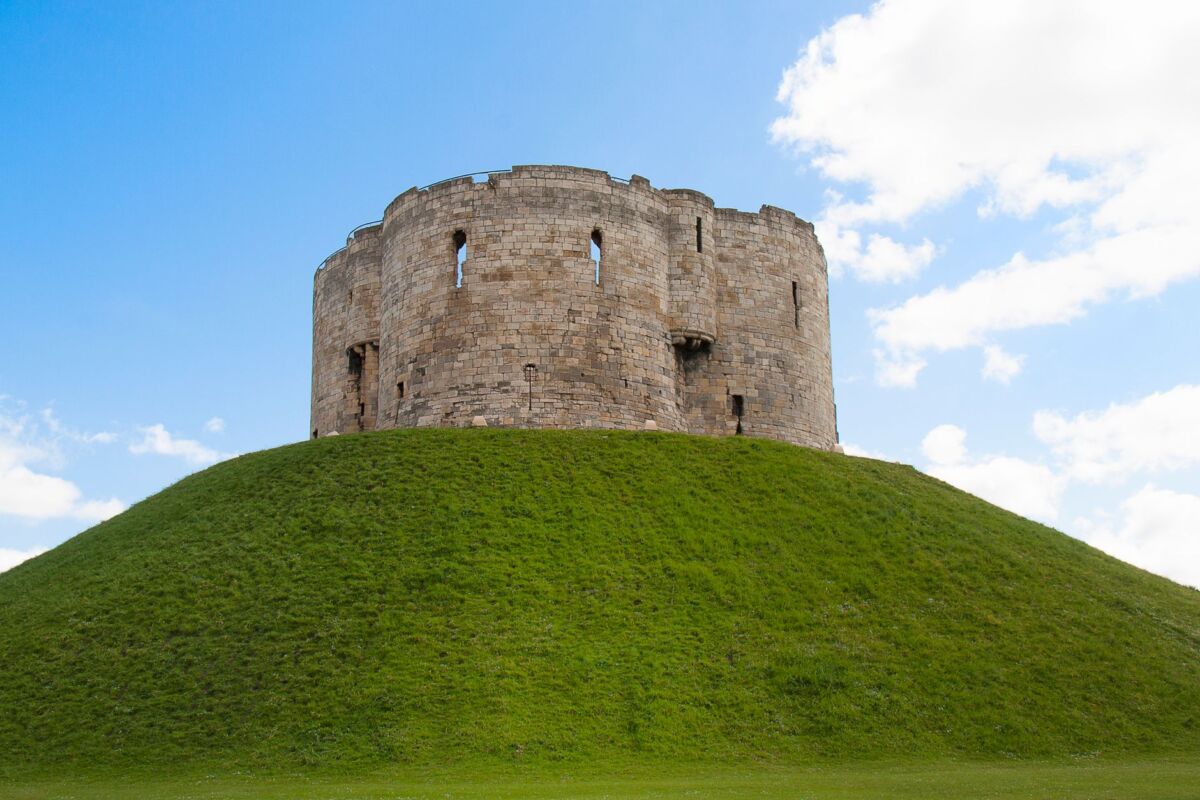 Historic Clifford's Tower on a grassy hill in York, England against a blue sky.